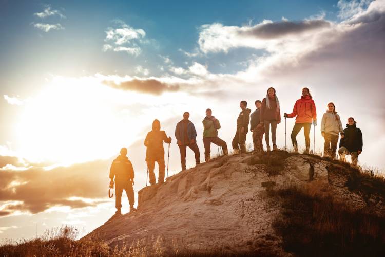 Big group of hikers stands against sunset. Hiking or trekking concept