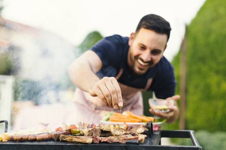 man smiling while seasoning meat on a grill