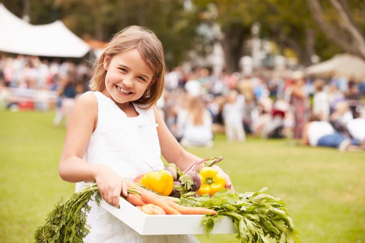little girl with a tray of fresh produce at an outdoor market