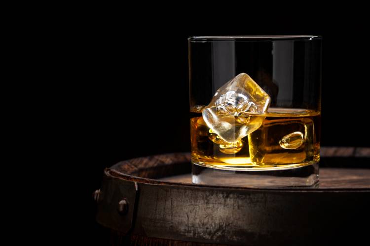 whiskey in a rocks glass. dark background and light shone on glass