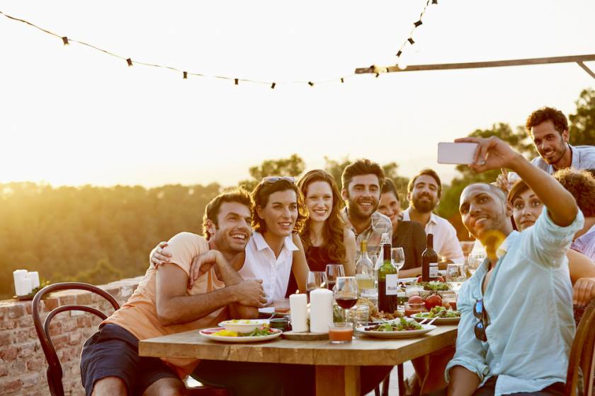 Smiling man taking group selfie on mobile phone at dinner party